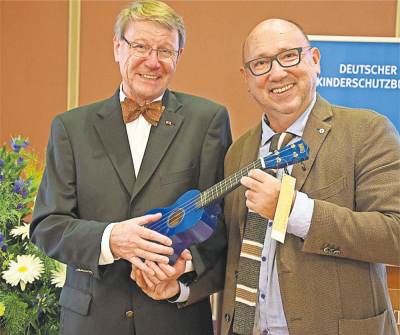 Foto: Johannes Schmidt (rechts), Vorsitzender des Kinderschutzbundes Niedersachsen, überreicht Dr. Henning Kehrberg, Vorsitzender des KSB in Stade, eine blaue Ukulele als "Geburtstagsgeschenk".